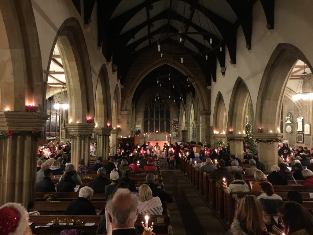 An aerial view of a church with people wearing Santa hats, and holding oranges with candles in them